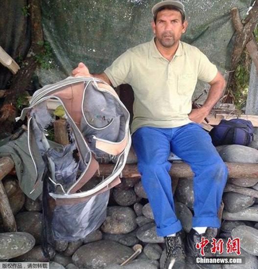 圖為當(dāng)?shù)貢r間7月30日，留尼旺島上的一名海岸清潔人員展示他找到的一個手提箱的殘骸。